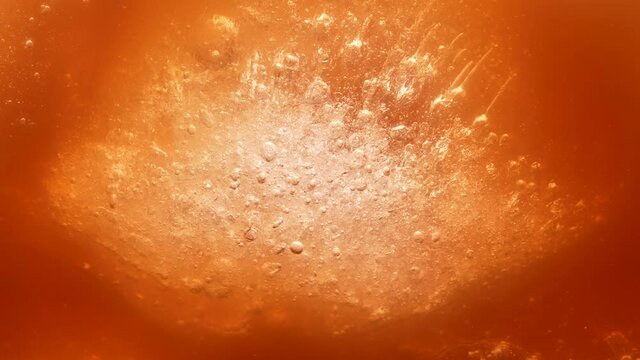 The ice cube lies in the caramel brown liquid and small bubbles float to the top. Slow motion. Close up.