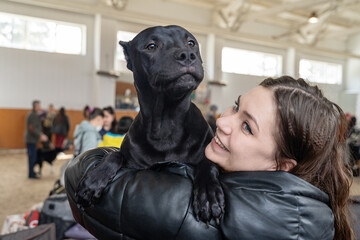 Young  laughing woman hugs black dog with funny face.