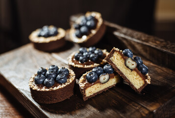 Chocolate tartlets decorated with blueberries on a dark wooden background. Beautiful portion cakes for the holiday table. Dessert with fresh blueberries.