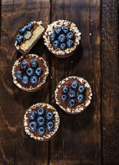 Chocolate tartlets decorated with blueberries on a dark wooden background. Beautiful portion cakes for the holiday table. Dessert with fresh blueberries, top view