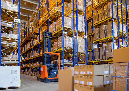 Interior of a modern warehouse storage with rows and goods boxes on high shelves. Pallet truck parking near shelves