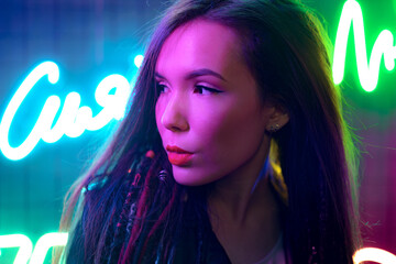 Portrait of a young attractive female standing near neon lamps at night