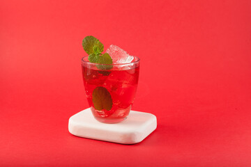 Red lemonade on red background, close-up. Glass of freshening summer soft drink with ice cubes
