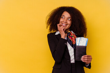 Young african american air hostess holding a plane tickets isolated on yellow background  relaxed thinking about something looking at a copy space.