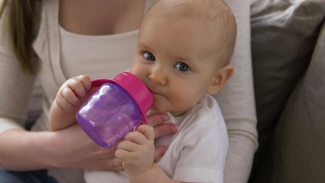 family, motherhood and people concept - close up of mother with little baby drinking water from sippy cup at home