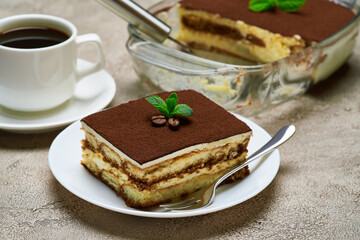 Traditional Italian Tiramisu dessert in glass baking dish and portion on grey concrete background