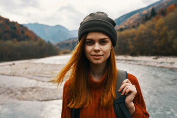beautiful woman in a sweater with a backpack in the mountains near the river in nature portrait