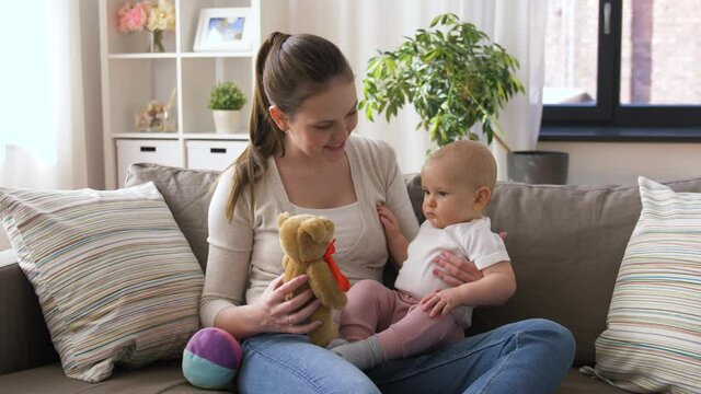family, motherhood and people concept - happy smiling mother and little baby playing with teddy bear toy at home - Powered by Adobe