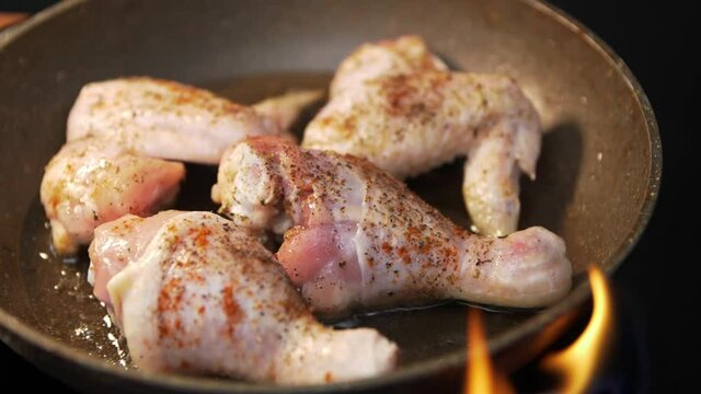 Close-up of chicken legs and wings fried in a pan in slow motion. Chicken legs and wings in spices are fried in a pan. Flashes of open fire in slow motion