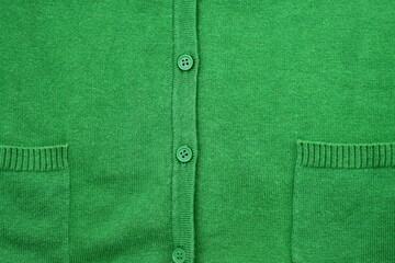 Part of a green sweater with pockets and a green button. Green knitted background with a button.