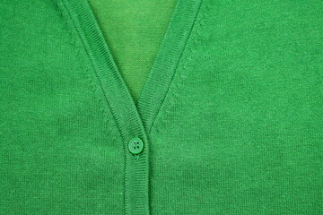 Part of a green sweater with a green button. Green knitted background with a button. 