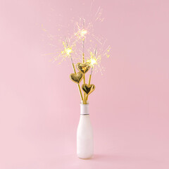 Celebration bottle with gold tubes with hearts. Spray bottle. Pastel pink background.