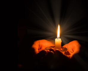 Hands holding a burning candle in dark room