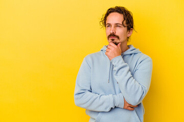 Young caucasian man isolated on yellow background looking sideways with doubtful and skeptical expression. - obrazy, fototapety, plakaty