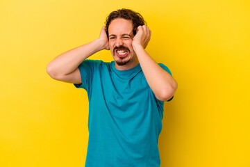 Young caucasian man isolated on yellow background covering ears with hands.