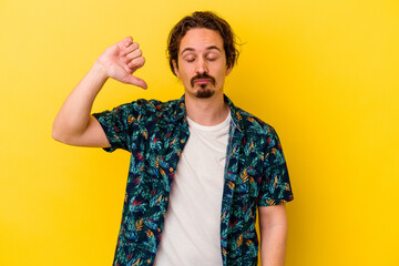 Young caucasian man isolated on yellow background showing a dislike gesture, thumbs down....