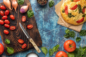 Top down view of a wooden cutting board with various raw vegetables used as toppings for a focaccia bread.