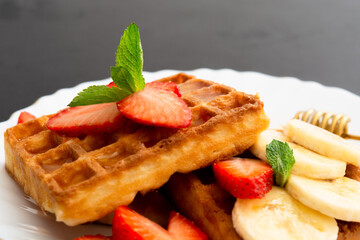 Closeup view of belgium waffles with strawberry and banana with mint on plate
