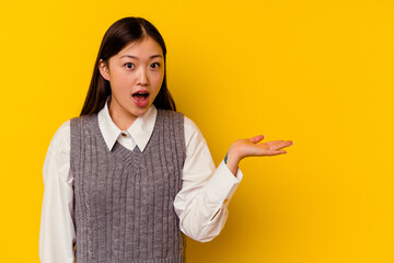 Young chinese woman isolated on yellow background impressed holding copy space on palm.