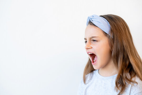 Naughty kid portrait. Temper tantrum. Child behavior problem. Troubled unhappy noisy little girl yelling with open mouth raising voice isolated on white empty space background.