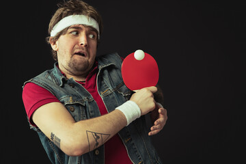 Young Caucasian funny man playing ping pong isolated on black background.
