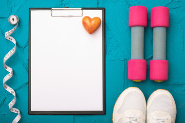 fitness at home - sheet of paper with a pen and white sneakers, dumbbells and measuring tape