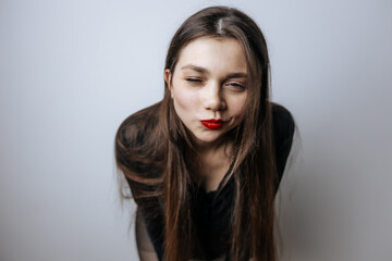 A beautiful girl with red lips winks. Large portrait on a light background