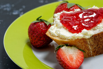 A slice of baguette, topped with cream cheese and strawberry jam. Served with fresh strawberries.