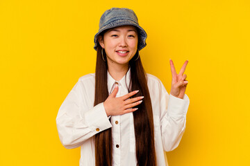 Young chinese woman isolated on yellow background taking an oath, putting hand on chest.