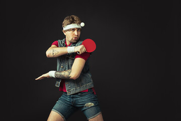 Young Caucasian funny man playing ping pong isolated on black background.