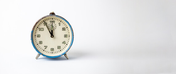 Old analog blue clock on a white background. The clock shows the time from five minutes to twelve o'clock. Copy Space. Clock. Time.