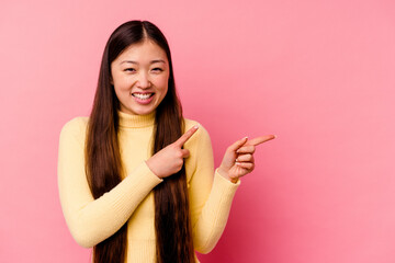 Young chinese woman isolated on pink background pointing with forefingers to a copy space,...