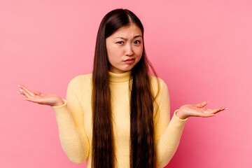 Young chinese woman isolated on pink background doubting and shrugging shoulders in questioning...