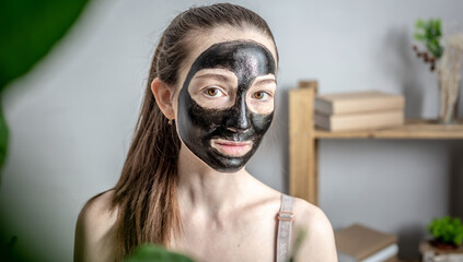 Portrait of a young woman with a cosmetic black mask on her face. Concept of cosmetic procedures, skin care with the use of natural cosmetics, lifestyle