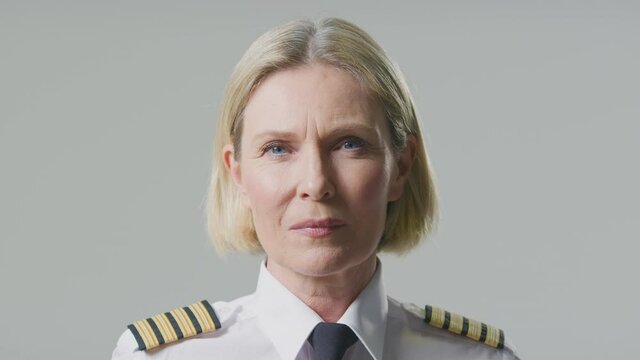 Serious mature female airline pilot or ship captain wearing uniform turning to face camera in front of plain studio background - shot in slow motion