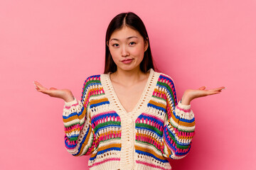 Young chinese woman isolated on pink background doubting and shrugging shoulders in questioning gesture.