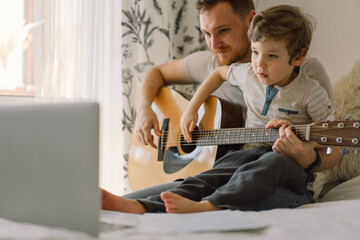 Father and son learn to play the acoustic guitar in an online lesson. Happy Father's day