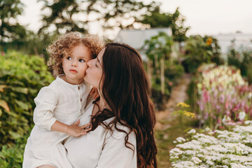 Fototapeta premium pretty curly daughter is walking with mom in the sunny park . The concept of summer holiday outdoors. Mother's, baby's day. Spending time together