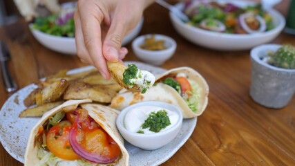 Healthy plant based lunch of wraps and potatoes on a side. Hand dipping a potato wing in the vegan mayo sauce. 