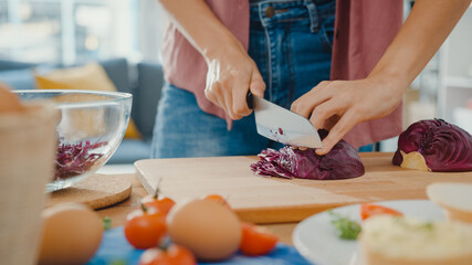 Obraz na płótnie Canvas Hand of young Asian woman chef hold knife cutting Red Chinese cabbage on wooden board on kitchen table in house. Cooking vegetable salad, Lifestyle healthy food eating and traditional natural concept.