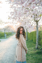 Portrait of a beautiful young woman in blooming sakura at sunset. Spring.