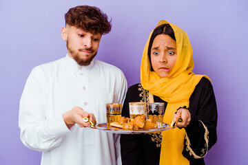 Young Moroccan couple drinking tea celebrating ramadan month isolated on purple background