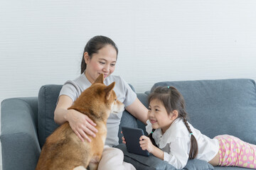 A mom and daughter is using a tablet computer and has a Shiba Inu on the sofa. Mom and baby.