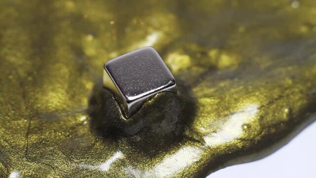 Gold magnetic plasticine envelops a metal iron magnet in the shape of a cube. Absorption of the magnet by a shiny trailing slime.