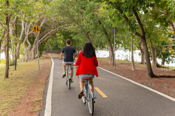 Back view of couple riding bicycles in the park.