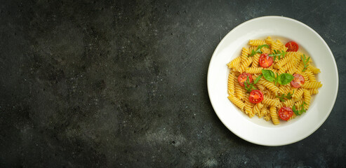 Food pasta on a dark background. Italian fusilli pasta with tomatoes, herbs and basil on a white plate. Healthy food concept.