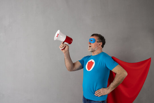 Senior man wearing superhero costume shouting through loudspeaker