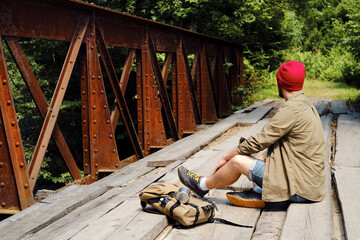 A man with a backpack on a wooden bridge against the backdrop of a beautiful mountain landscape with trees. Hike along the hiking trail. Travel and exploration. Healthy lifestyle, active rest