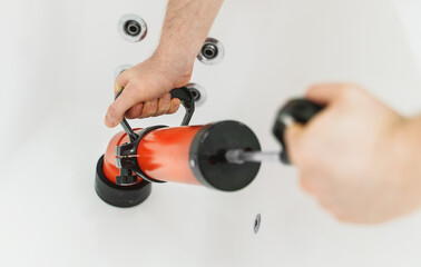 Plumber unclogging bathtub with professional force pump cleaner.