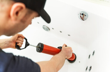 Plumber unclogging bathtub with professional force pump cleaner.